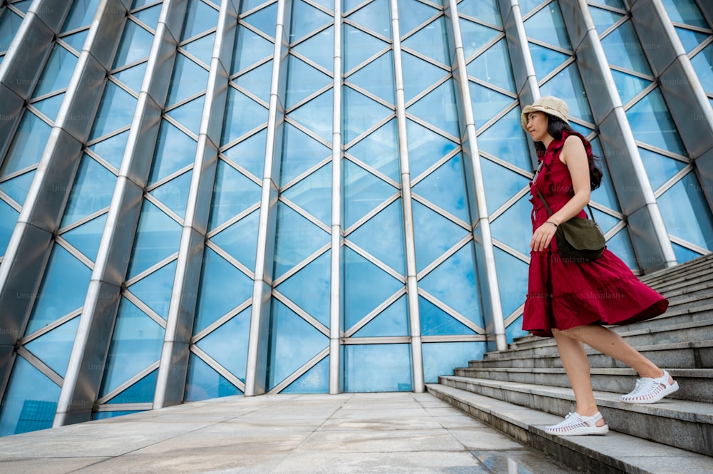 Donna asiatica in vestito rosso all'edificio moderno, ragazza femminile con lo stile di vita urbano della città