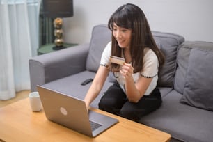 Una giovane bella donna sta usando la carta di credito per lo shopping online sul sito web a casa, concetto di e-commerce