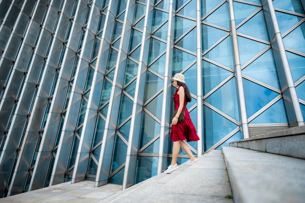 Mulher asiática no vestido vermelho no edifício moderno, menina feminina com estilo de vida urbano da cidade