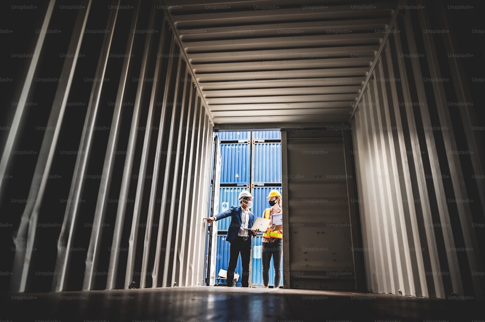 Businessman, executives and engineers wear medical face masks and helmet, While inspecting industrial plants and warehouses for international shipping businesses Concepts of import and export