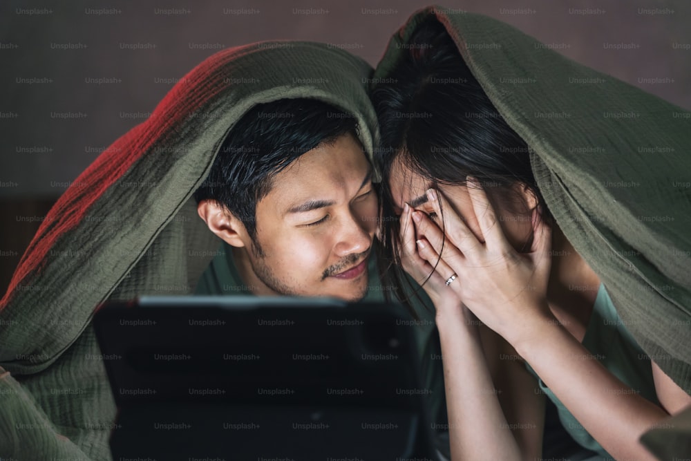아시아 성인 애인 결혼 부부는 집에서 침대에 담요에 노트북이나 태블릿에서 공포 온라인 영화를 보는 것을 즐깁니다., 가정 격리 격리 lifetyle