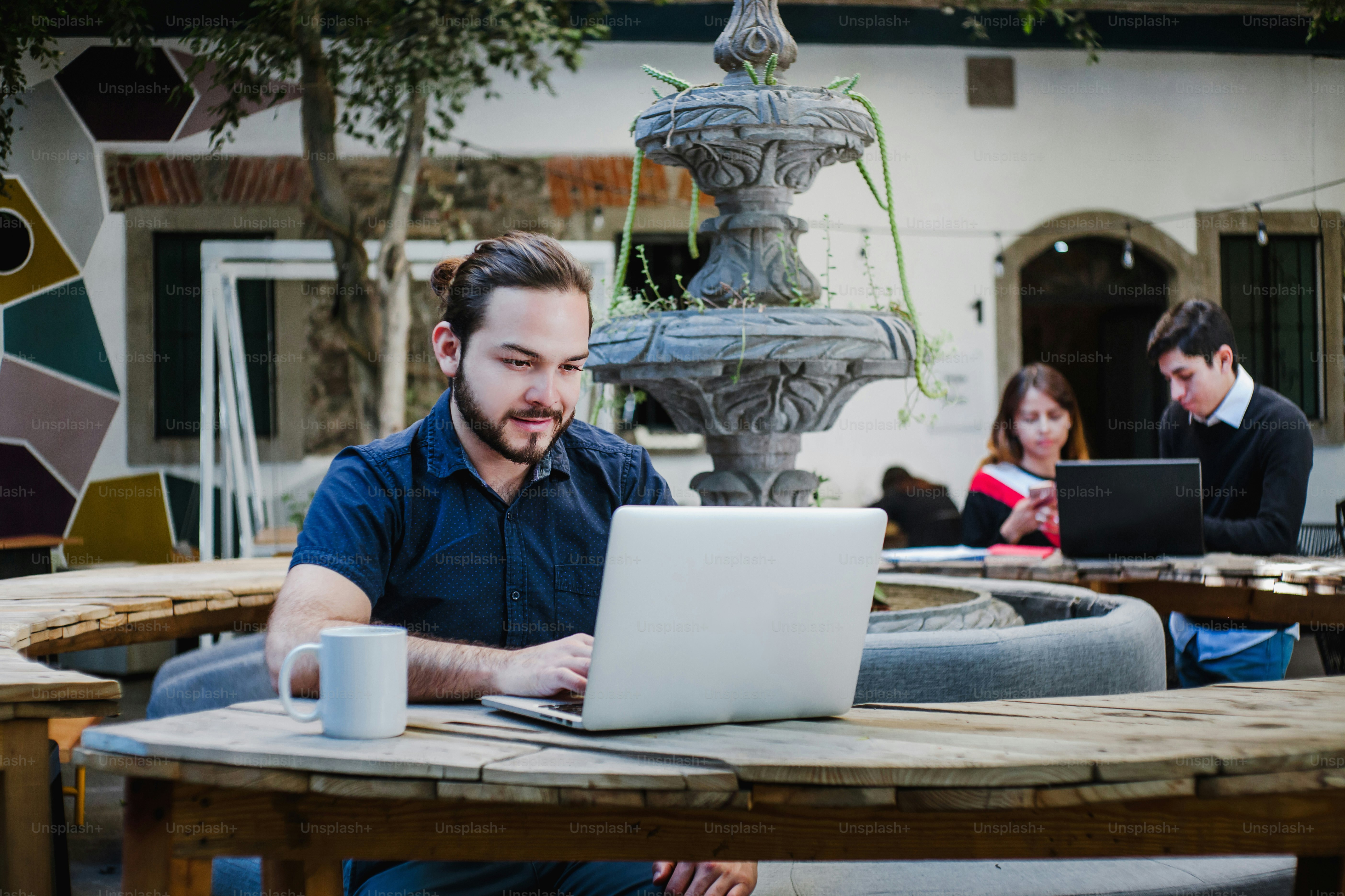 Young hispanic college student working on computer while sitting at university yard