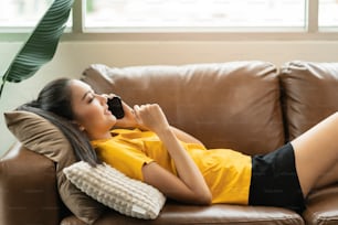 happiness cheerful smiling young adult asian female woman wear yellow cloth hand conversation on smartphone on sofa at home remote quarantine lock down period home interior background