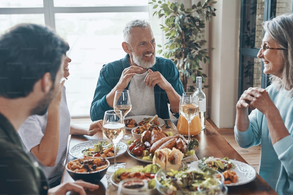 Familia multigeneracional sonriente disfrutando de una deliciosa cena mientras está sentada en el moderno apartamento