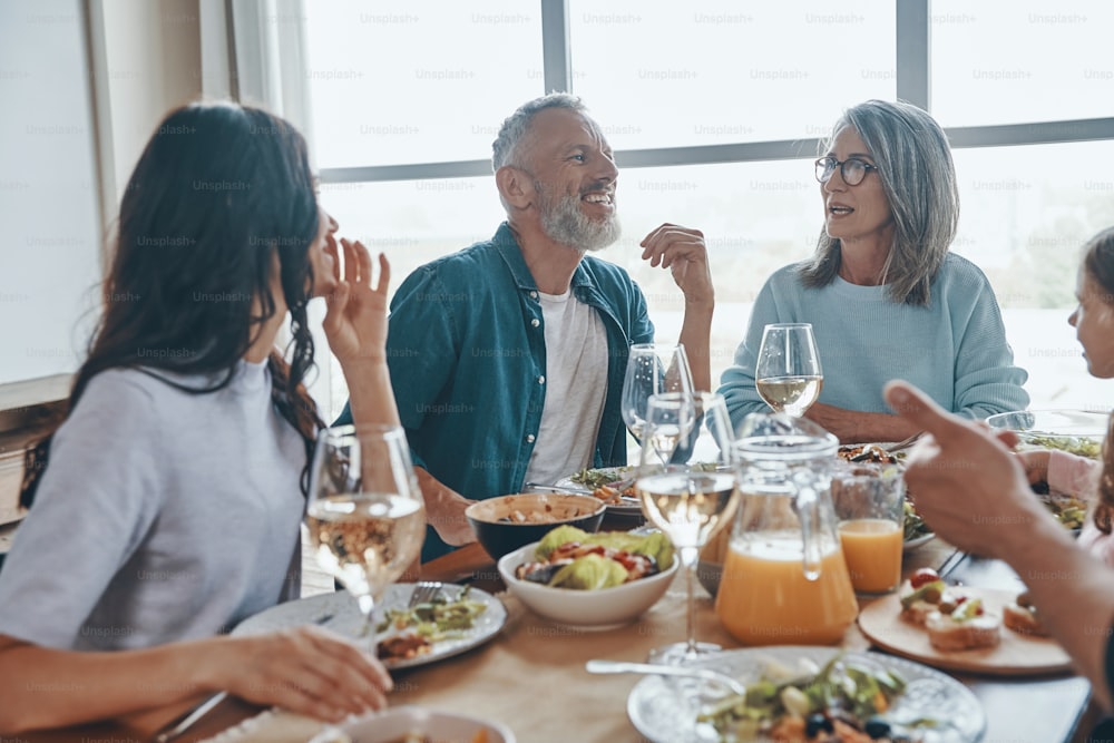Familia multigeneracional feliz que se comunica y sonríe mientras cenan juntos