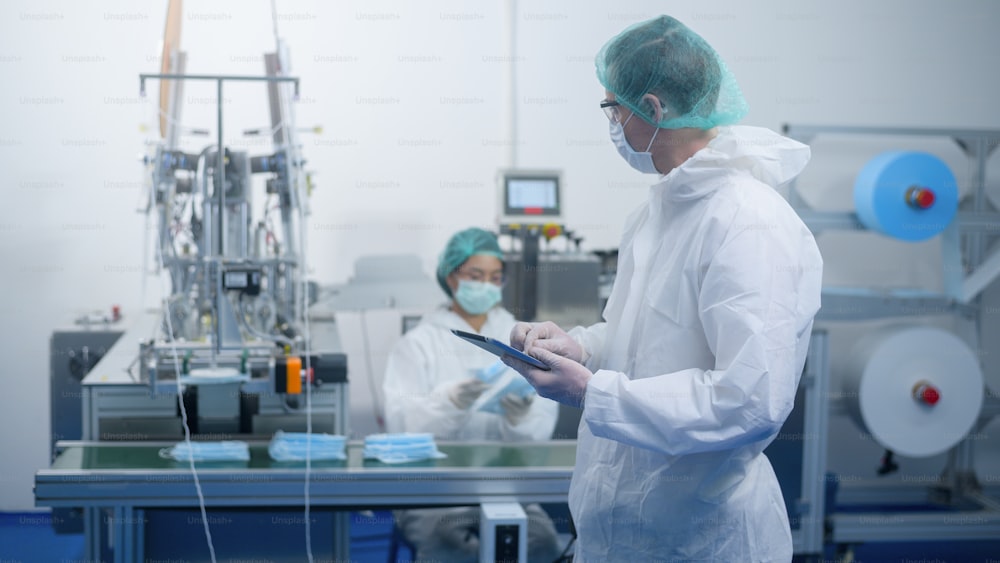 Lavoratori che producono maschere chirurgiche in una fabbrica moderna, protezione Covid-19 e concetto medico.