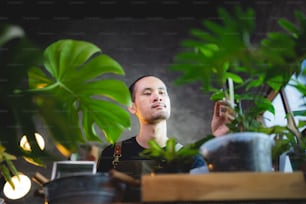 젊은 아시아 남자는 집에서 작은 녹색 정원에서 식물을 재배하고, 집에서 녹색 자연과 함께 취미 생활 방식을, 화분에 꽃 나무를 식물원 원예 농업 재배에 만족합니다.