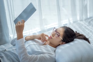 Young asian woman lying using tablet on bed at home.