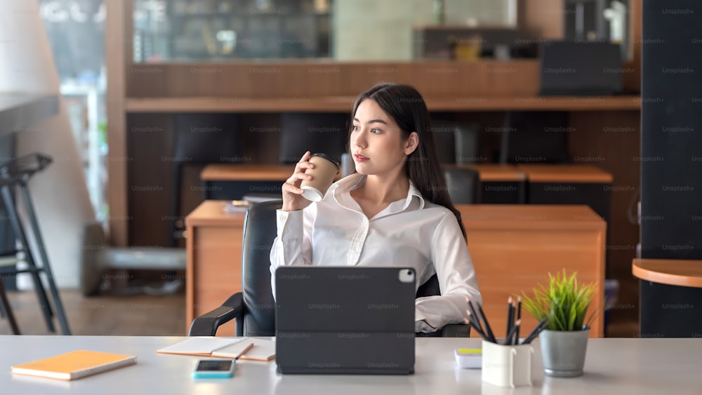 Young Asian businesswoman sitting relaxed drinking coffee with tablet at the office.