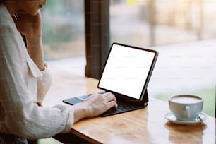 모의. 태블릿 빈 화면에 손으로 인쇄하는 여자. 사무실 테이블에 놓인 커피 머그잔.