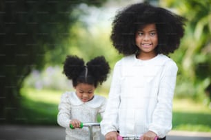 아프리카계 미국인 형제, 거리에서 스쿠터를 타는 여동생을 가르치는 형제, 가족 개념, 아이들은 스쿠터로 야외에서 놀고, 어린이를 위한 활동적인 레저 및 야외 스포츠.