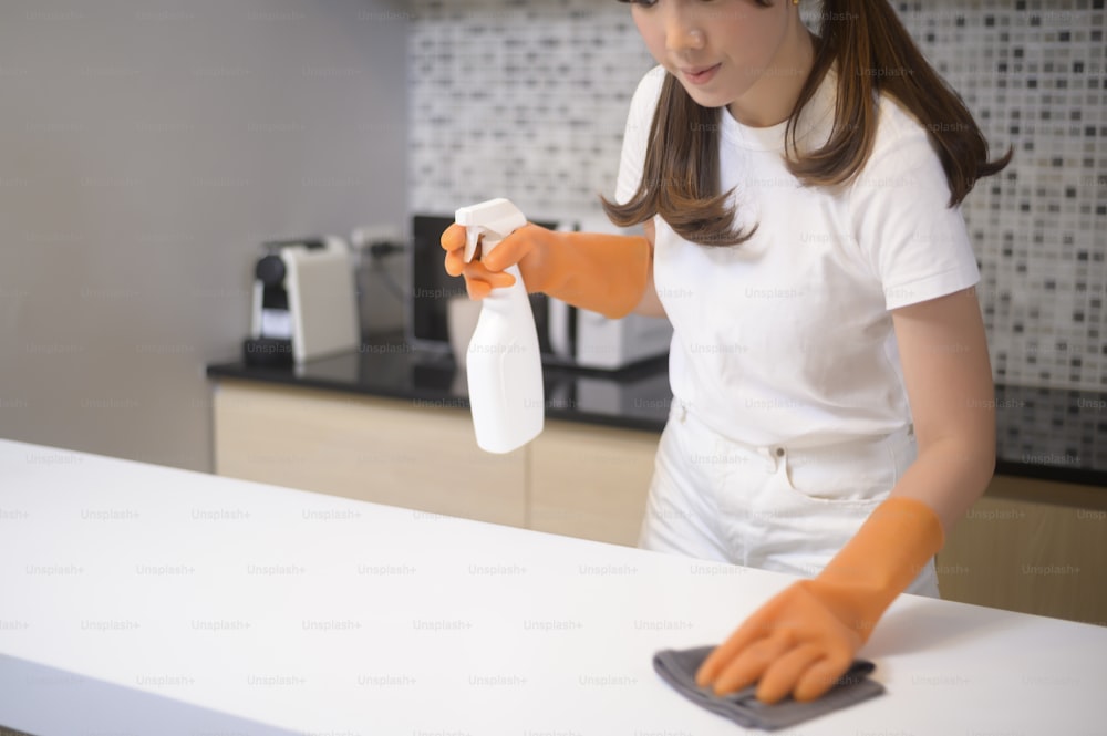 A young beautiful woman wearing protective rubber gloves is cleaning table in kitchen at home.
