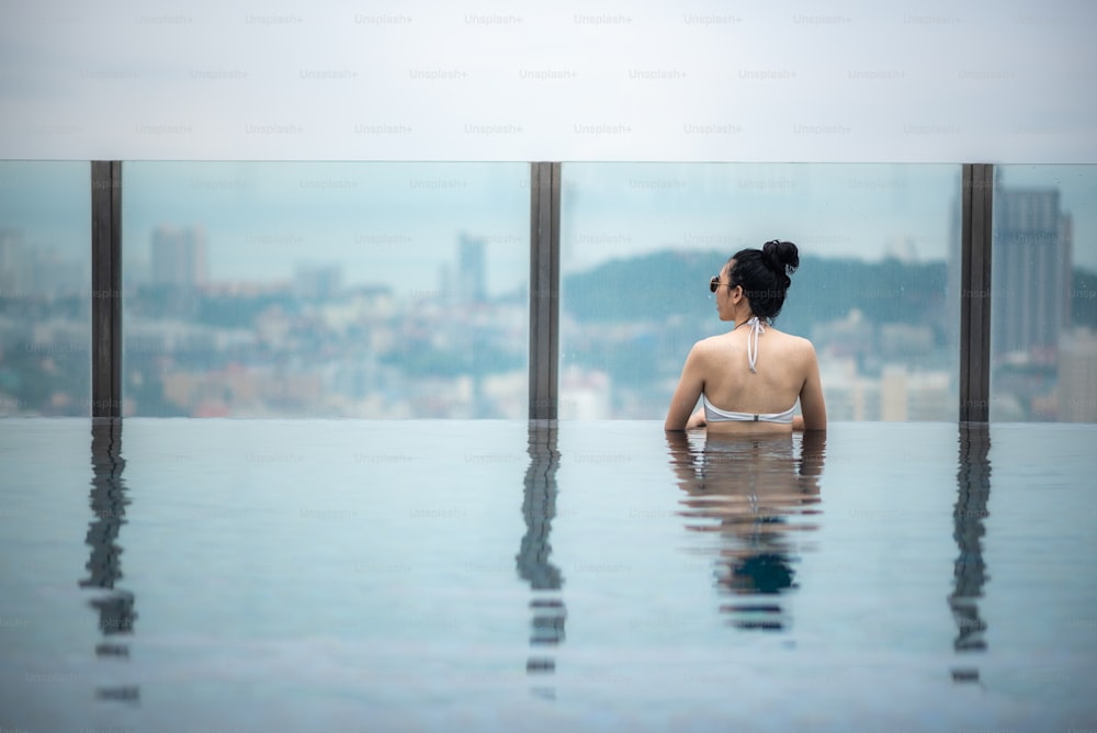 Conceito de viagem asiática. mulher nova que aprecia com a vista do céu da cidade da piscina do telhado do hotel, estilo de vida bonito da menina ao ar livre no tempo de férias