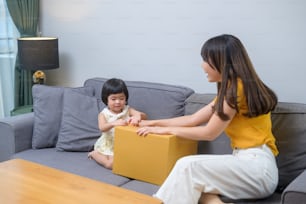 Una mamá feliz con una hija abriendo una caja de cartón en la sala de estar de casa