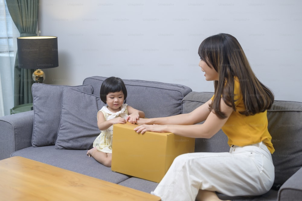 A happy mom with daughter opening cardboard box in living room at home