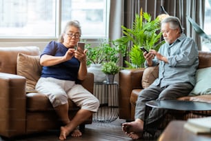 happiness asian retired couple enjoy playing and competition game smartphone mobile online together on sofa in living room home interior background,asian couple playing game together home isolate idea