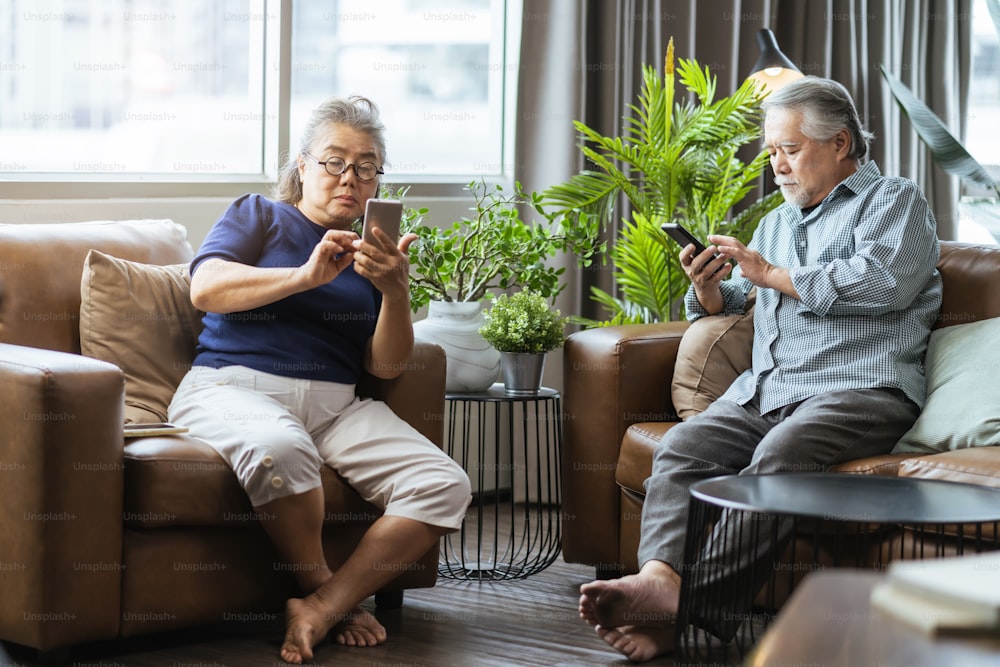 happiness asian retired couple enjoy playing and competition game smartphone mobile online together on sofa in living room home interior background,asian couple playing game together home isolate idea