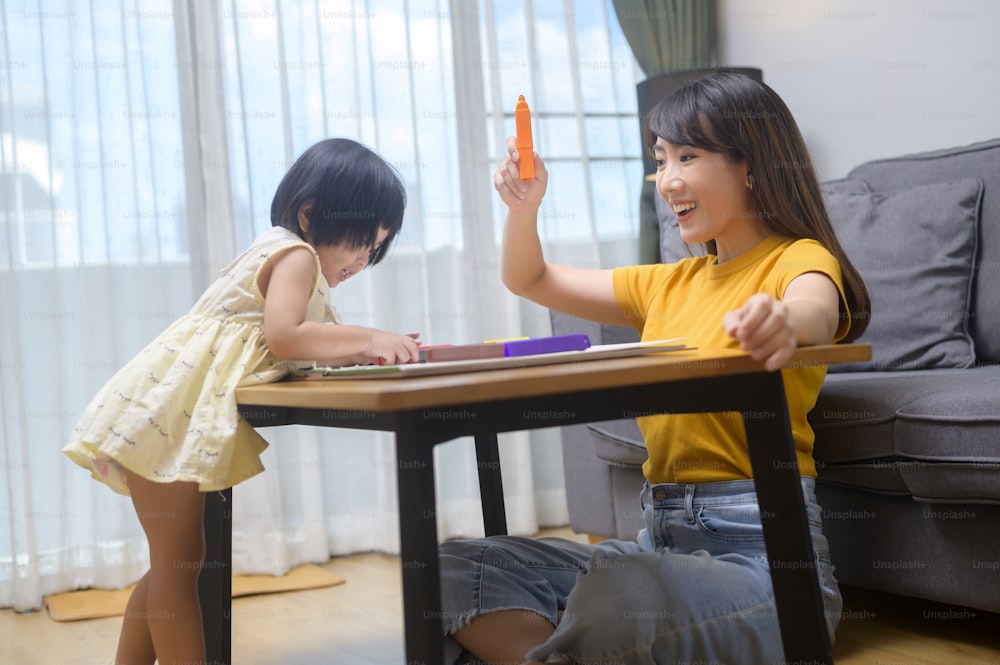 自宅のリビングで色鉛筆で絵を描く娘を手伝う若いお母さん。
