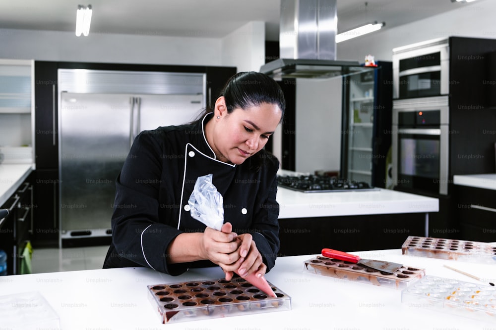 mulher latina chef confeiteiro vestindo uniforme preto no processo de preparação de deliciosos chocolates doces na cozinha no México América Latina