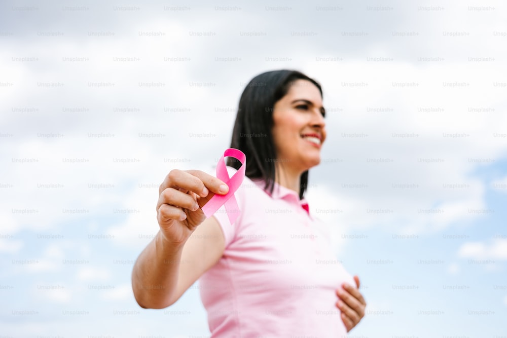 retrato de la mano de la mujer latina sosteniendo cintas rosadas de concientización sobre el cáncer de mama con el cielo azul como fondo en América Latina