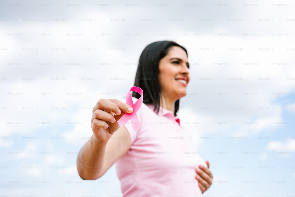 portrait of latin woman hand holding pink breast cancer awareness ribbons with blue sky as background in Latin America