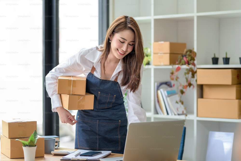 Beautiful young Asian business owner woman prepare parcel box and check online orders of product for deliver to customer. Shopping Online concept.