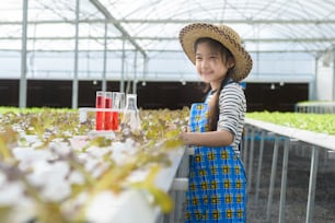 Ein glückliches süßes Mädchen, das in hydroponischer Gewächshausfarm, Bildung und Wissenschaftlerkonzept lernt und studiert