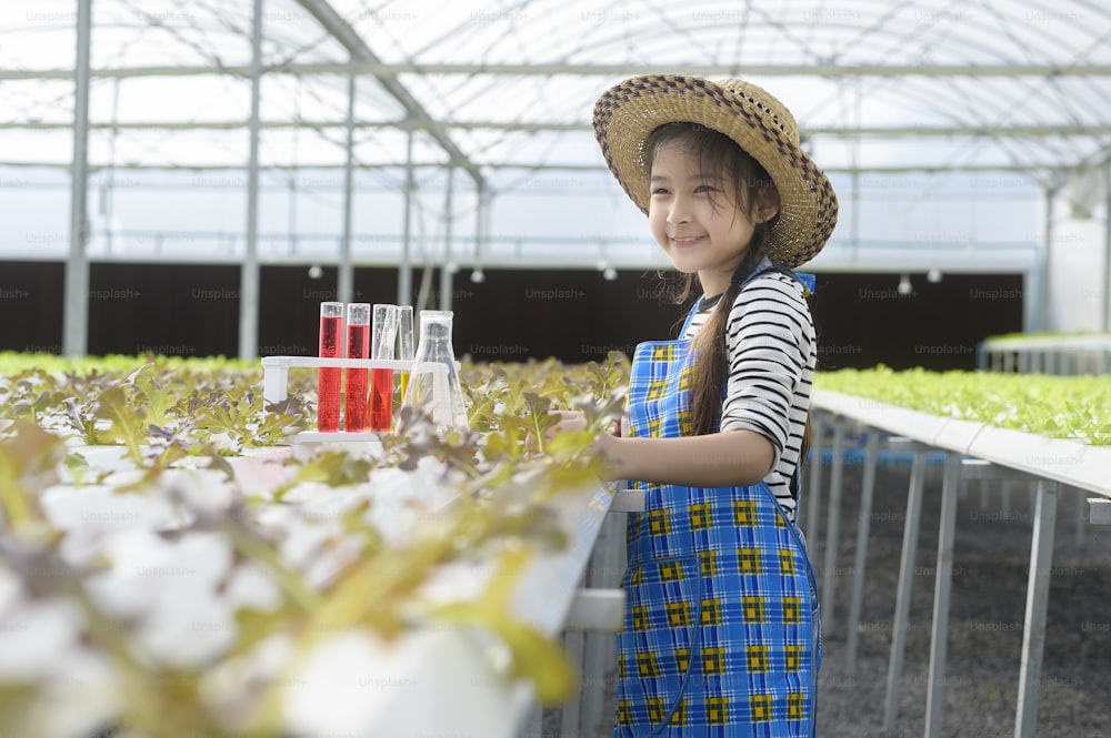 Uma menina bonita feliz aprendendo e estudando na fazenda de estufa hidropônica, educação e conceito de cientista