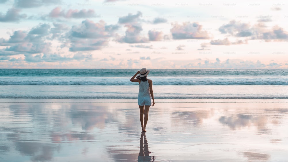 Vista trasera de la mujer asiática turista adulta joven que camina relajada en la arena de la playa con un hermoso cielo dramático de la puesta del sol. Viajes nacionales al aire libre en el océano de Andamán. Phuket, Tailandia.