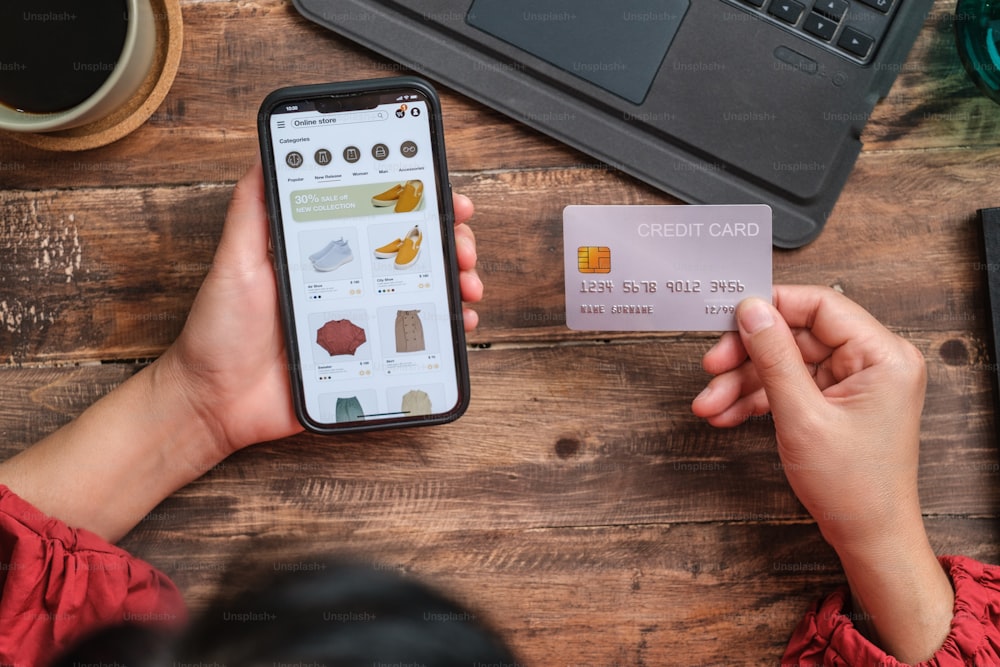 Nahaufnahme Frau Hand mit Kreditkarte Shopping online auf Mobile App auf Holztisch zu Hause