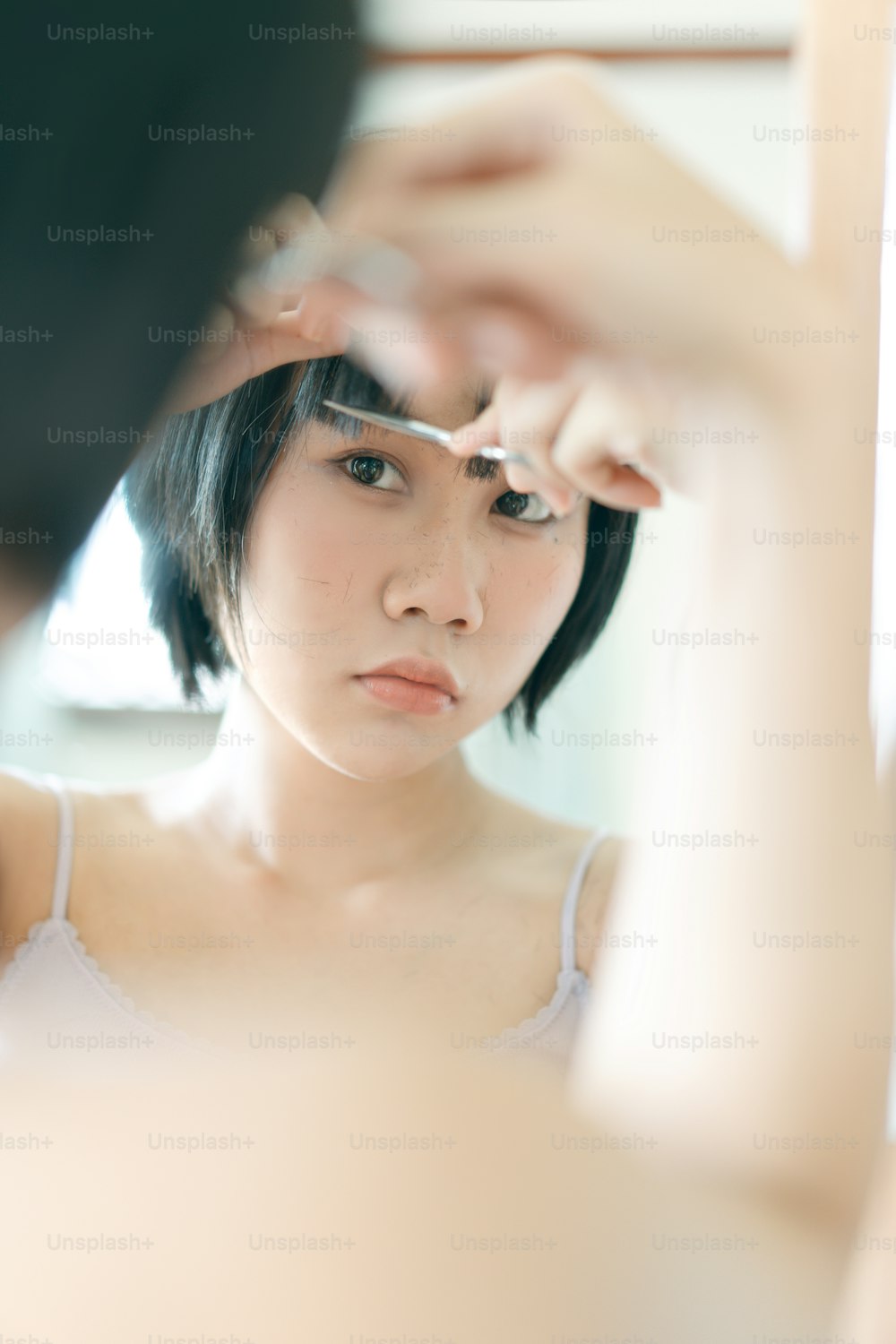 Concepto de quedarse en casa con estilo de vida de cuarentena. Mujer asiática adulta joven autocortada flequillo corte de pelo con tijeras. Ojos mirando a un espejo. Fondo en el día con la luz de la naturaleza.