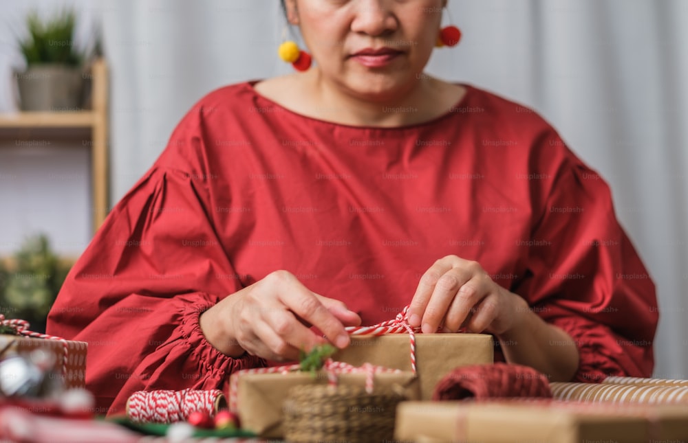 mulher que faz a caixa de presente artesanal do Natal com deformação de papel marrom com decoração de xmas na mesa de madeira