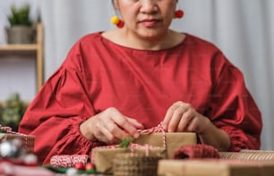 Frau macht Weihnachten handgemachte Geschenkbox mit braunem Papier Warpping mit Weihnachtsdekor auf Holztisch