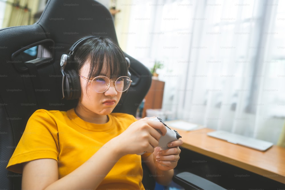 괴짜 스타일의 젊은 성인 아시아 게이머 여성은 안경을 쓰고 온라인 게임을 합니다. 승리 분위기를위한 경쟁. 사람들은 집에서 여가 라이프 스타일을 즐깁니다.