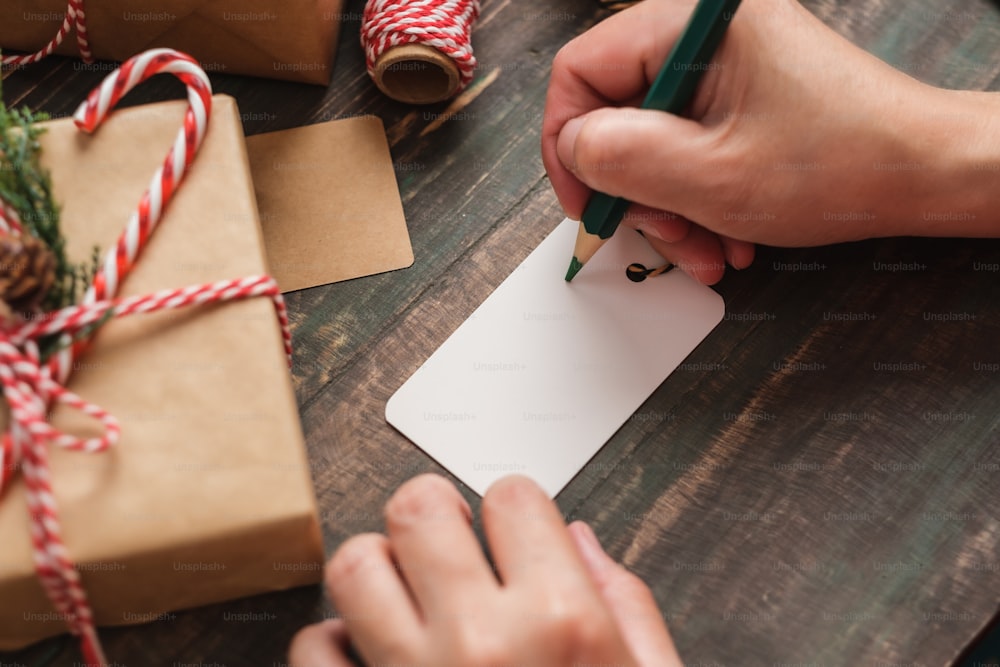 Mujer que escribe la etiqueta del regalo y la adjunta al regalo de Navidad en la mesa de madera