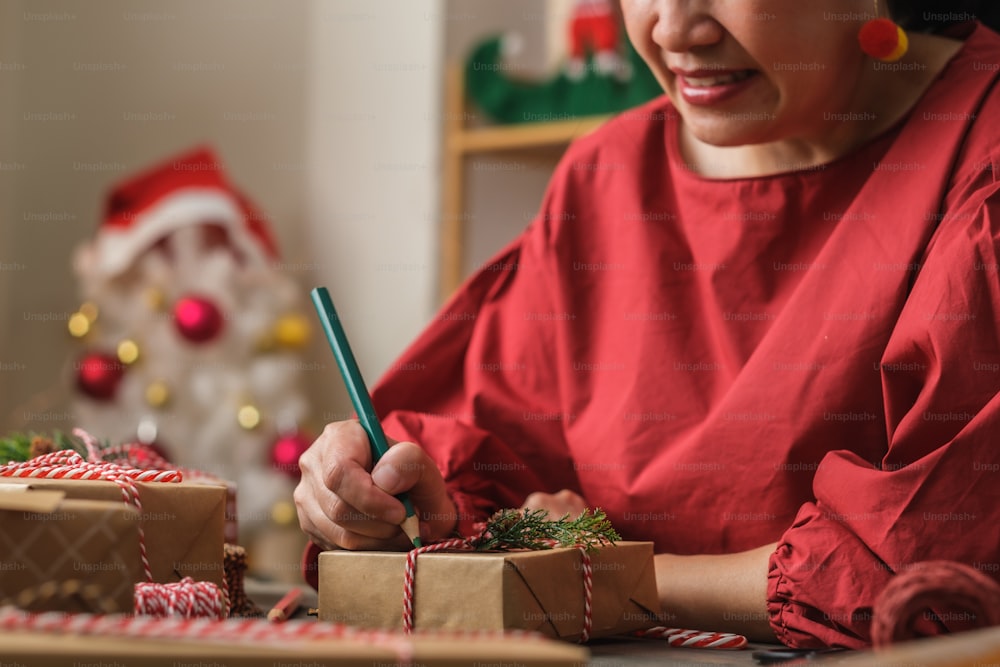 Frau schreibt Geschenkanhänger und befestigt an Weihnachtsgeschenk auf Holztisch