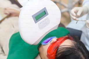 A woman wearing protective glasses  examining by stomatologist , Tooth whitening by ultraviolet lamp