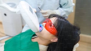 Eine Frau mit Schutzbrille untersucht durch Stomatologen, Zahnaufhellung durch UV-Lampe