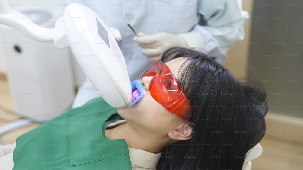 Una mujer con gafas protectoras examinando por el estomatólogo, Blanqueamiento dental por lámpara ultravioleta