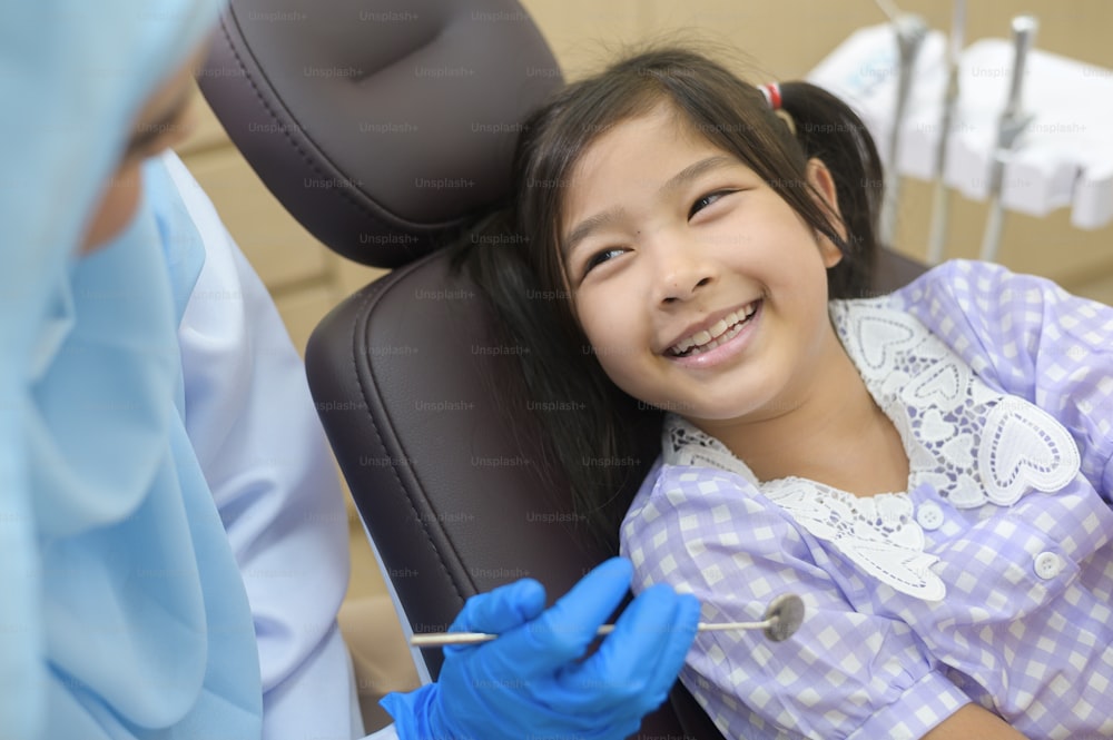 Une petite fille mignonne ayant des dents examinées par un dentiste musulman dans une clinique dentaire, un examen des dents et un concept de dents saines