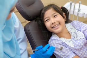 Ein kleines süßes Mädchen, das Zähne von einem muslimischen Zahnarzt in der Zahnklinik untersuchen lässt, Zahnuntersuchung und Konzept für gesunde Zähne