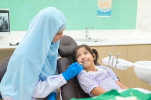 Una piccola ragazza carina che si fa esaminare i denti dal dentista musulmano in clinica dentale, controllo dei denti e concetto di denti sani