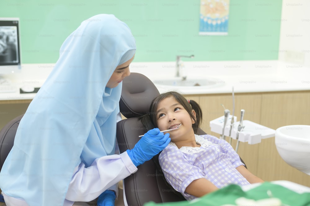 A little cute girl having teeth examined by muslim dentist in dental clinic, teeth check-up and Healthy teeth concept