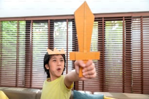 Kleiner kleiner Junge Kind spielen Ritter Halten Schwert aus Pappe Anspruch auf mittelalterliche Zeit Kampf mit aufgeregt und fröhlich im Wohnzimmer zu Hause, kleiner Junge spielt Kampf Familie Wochenende Lebensstil