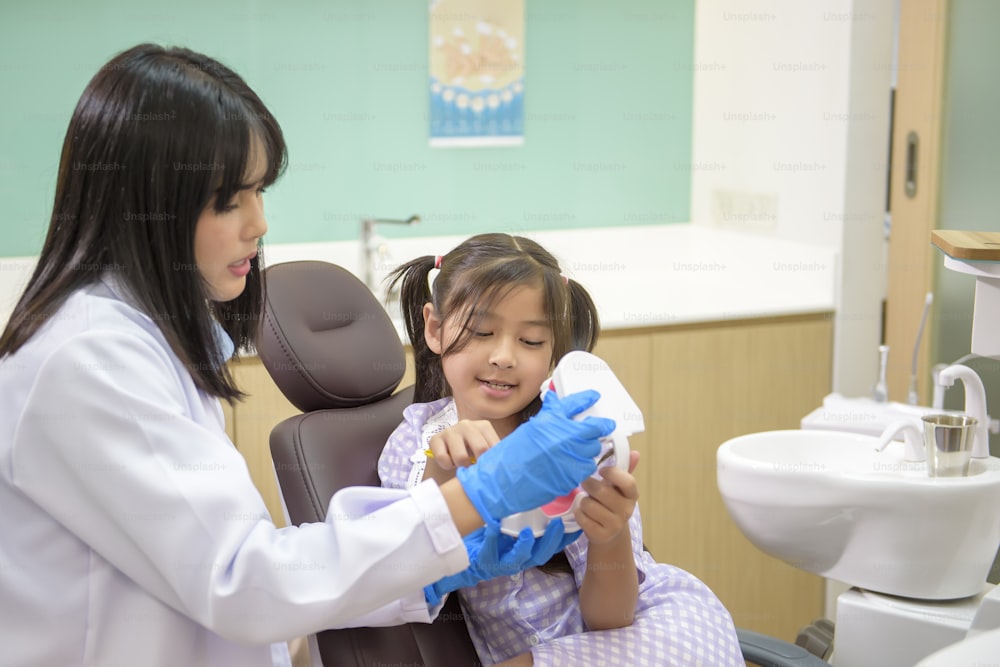 歯科医院で小さな女の子に歯磨きの仕方を実演する女性歯科医、歯の検診、健康な歯のコンセプト