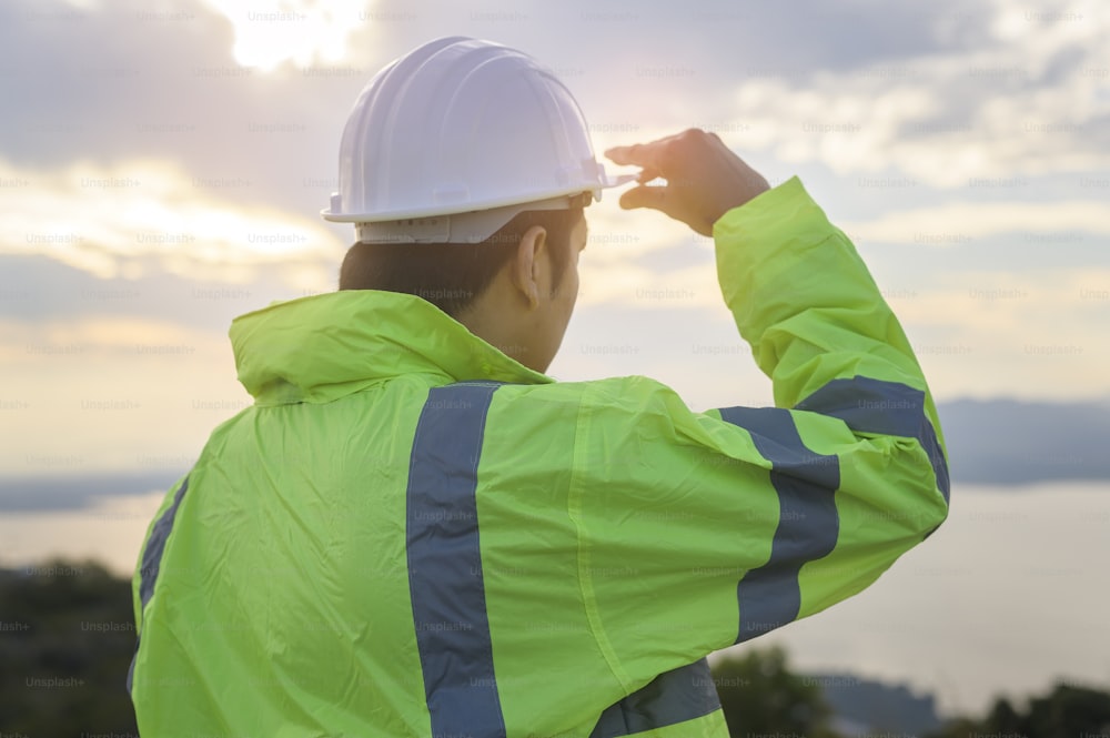 a man engineer is putting a protective helmet on her head at sunset.