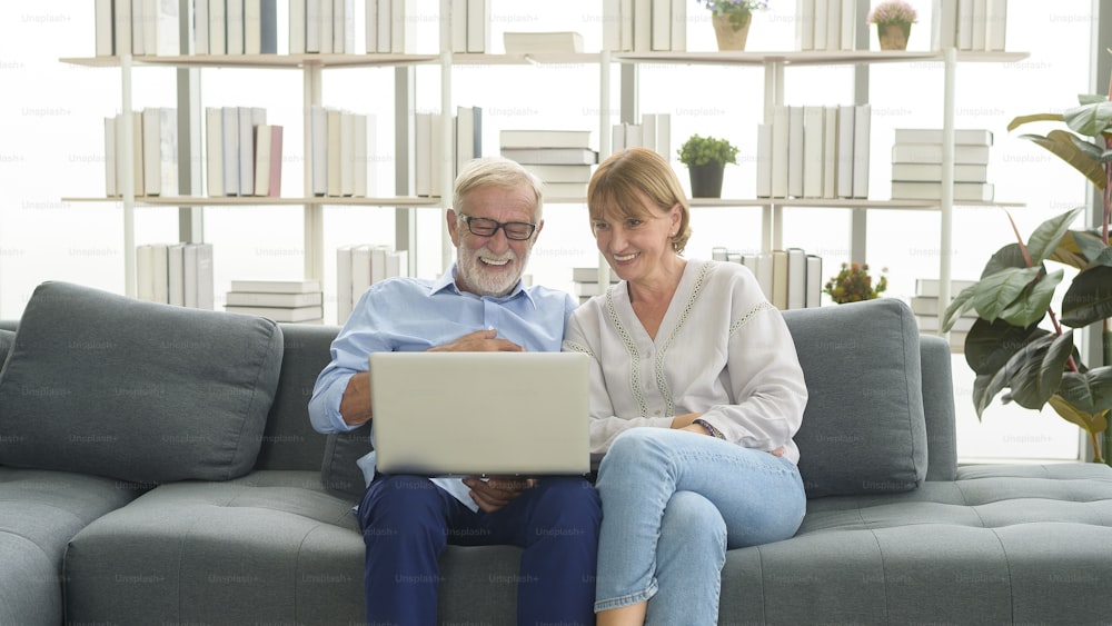 Feliz pareja de ancianos caucásicos usando computadora portátil en casa
