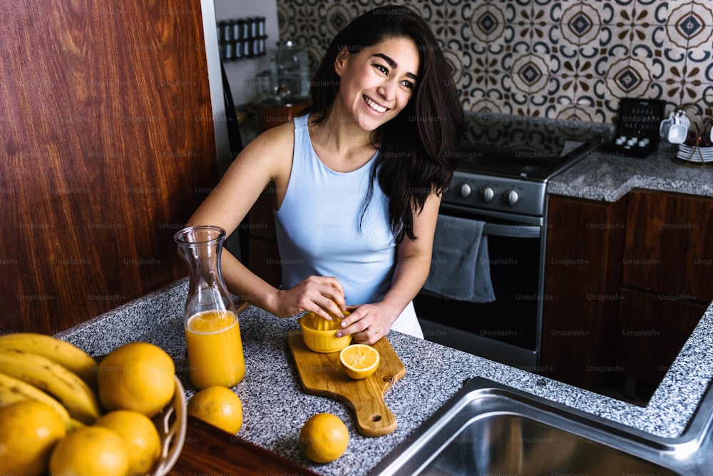 Hispanic brunette young latin woman preparing orange juice at the kitchen in Mexico Latin America