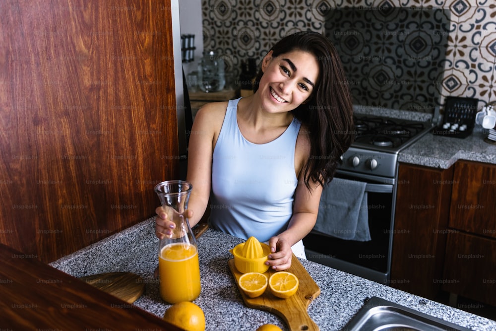 히스패닉 갈색 머리 젊은 라틴 아메리카 멕시코 부엌에서 오렌지 주스를 준비 하는 젊은 라틴 여자