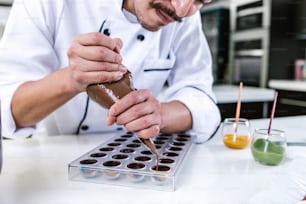 latin man pastry chef wearing uniform in process of preparing delicious sweets chocolates at kitchen in Mexico Latin America